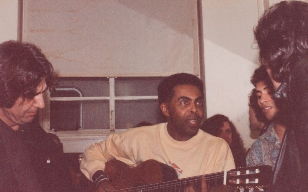 Gilberto Gil segura violão em sala com várias pessoas